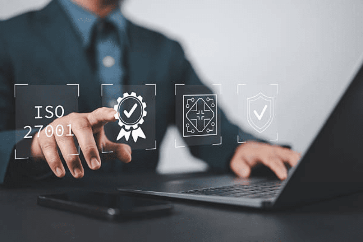 Main désignant des pictogrammes ISO 27001 au-dessus d'un ordinateur portable